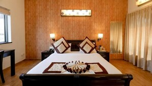 A hotel room with a wooden paneled wall, a large bed with a decorative headboard, two bedside tables with lamps, and a window with curtains. - La Sunila Suites (Arpora)