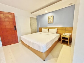 Ein Hotelzimmer mit Bett, Holz-Kopfteil, Nachttisch mit Telefon und Tür mit Nummernschild.