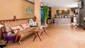Eine Hotelhalle mit einer Couch, einem Couchtisch, einer Rezeption und einer großen Pflanze.