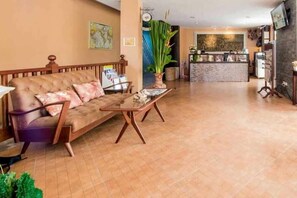 Un vestíbulo de hotel con un sofá, una mesa de centro, una recepción y una planta grande.