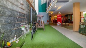 Eine Hotelhalle mit Kunstrasen, einem Fahrrad, einer Holzschaukel und einem roten Schild, das eine mobile App bewirbt.