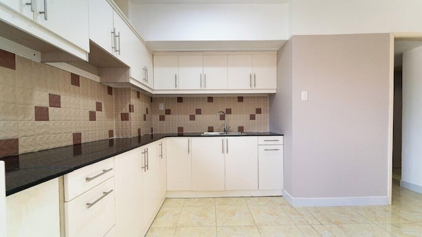 A kitchen with white cabinets, a black countertop, and a tiled backsplash. - Nam Hai Hotel (Phan Thiet)