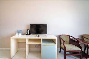A room with a white desk, a television, a small refrigerator, two wooden chairs, and a water bottle on the desk. - NAM HAI Hotel (Phan Thiet)