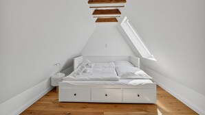 Un letto bianco in una stanza con soffitto spiovente e pavimento in legno.
