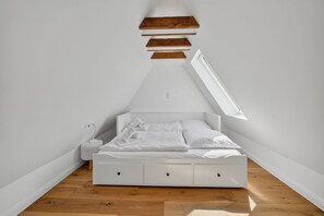 A white bed in a room with a slanted ceiling and wooden flooring. - Hüs lepen Will - Stylish vacation home for 4 people with sauna, garden and (Hörnum (Sylt))