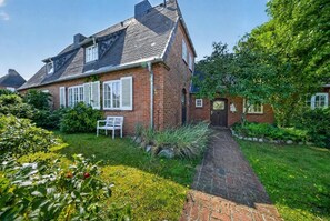 Une maison en briques avec un jardin et un chemin qui mène à l’entrée.