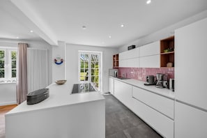 A modern kitchen with white cabinetry, a central island, and a pink backsplash. - Hüs lepen Will - Elegant vacation home for 4 with a sauna, garden, and (Hörnum (Sylt))
