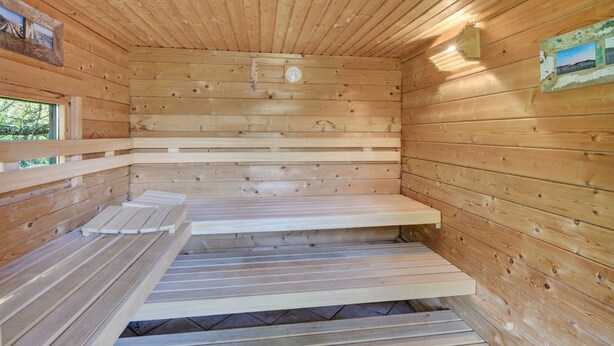 Una stanza sauna con pareti in legno, panche e un termometro fissato al muro.
