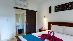 Une chambre d’hôtel avec un lit, une table de chevet, un climatiseur fixé au mur, une porte et une salle de bain visible à travers une porte ouverte.