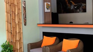 Un espace de vie aménagé avec des meubles en osier, une table basse en verre et un téléviseur à écran plat fixé au mur.
