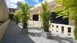 Un espace extérieur abrité, doté d’un sol en gravier, de plantes en pot et d’un bâtiment avec de grandes fenêtres et des balcons.