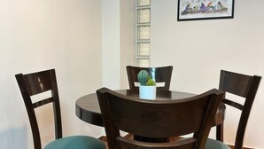 A round dining table with four dark wooden chairs, each with teal cushions. A small white pot with a green plant is on the table. - Brand new apartment with private jacuzzi. (Cusco)