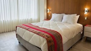 A neatly made bed with a quilted cover, two bedside tables with lamps, and a window with sheer curtains. - Brand new apartment with private jacuzzi. (Cusco)