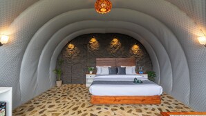 A bedroom with a stone-patterned floor, a wooden bed frame, a stone wall, and a hanging light fixture.