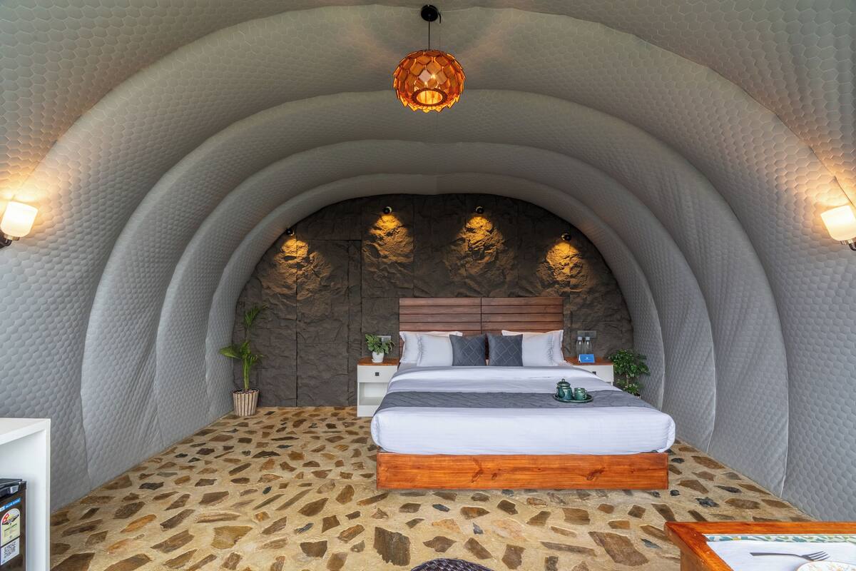 A bedroom with a stone-patterned floor, a wooden bed frame, a stone wall, and a hanging light fixture.