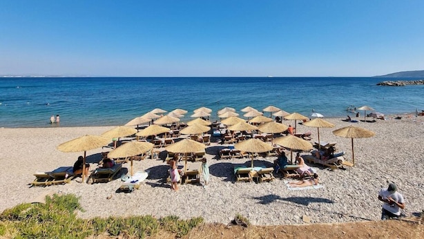 A beach with sun loungers and umbrellas, a clear blue sky, and calm sea.