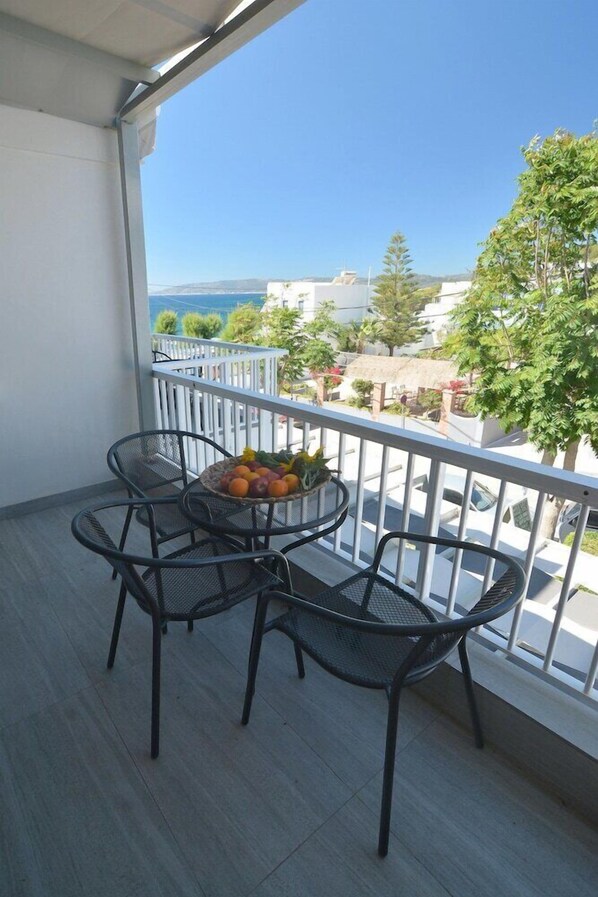 A balcony with a table and chairs, a bowl of fruit, and a view of the sea and buildings. - Ilioxenia (Chios)