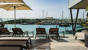 A terrace with sun loungers and a view of a marina with boats. - Strand Suites By Neu Collective (Gzira)