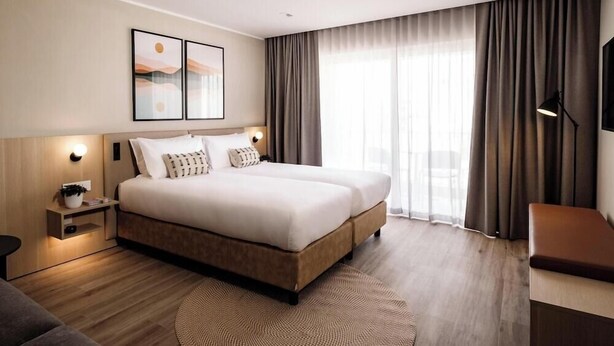 A modern hotel room with a large bed, a bedside table, a lamp, and a TV. - Strand Suites By Neu Collective (Gzira)