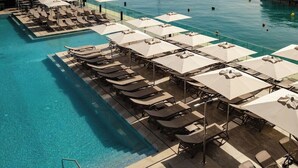 A poolside area with sun loungers and umbrellas, a clear pool, and a view of boats in the water. - Strand Suites By Neu Collective (Gzira)