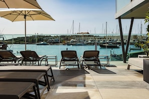 A terrace with sun loungers and a view of a marina with boats. - Strand Suites By Neu Collective (Gzira)