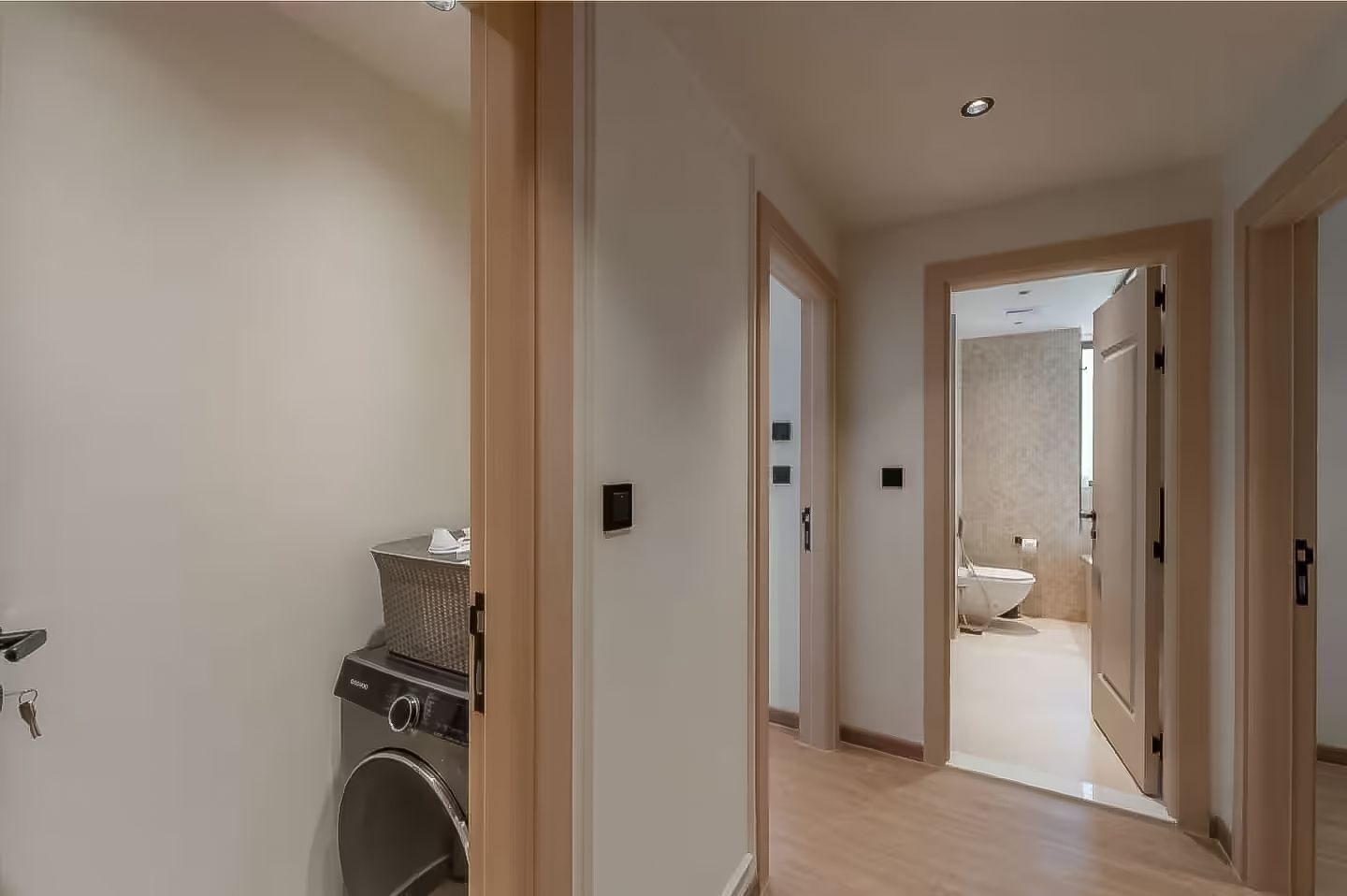 A hallway leading to a bathroom with a washing machine and a small table with items on it.