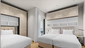 Moderni hotellihuone, jossa on kaksi sänkyä, suuri ikkuna ja pelkistetty sisustus.