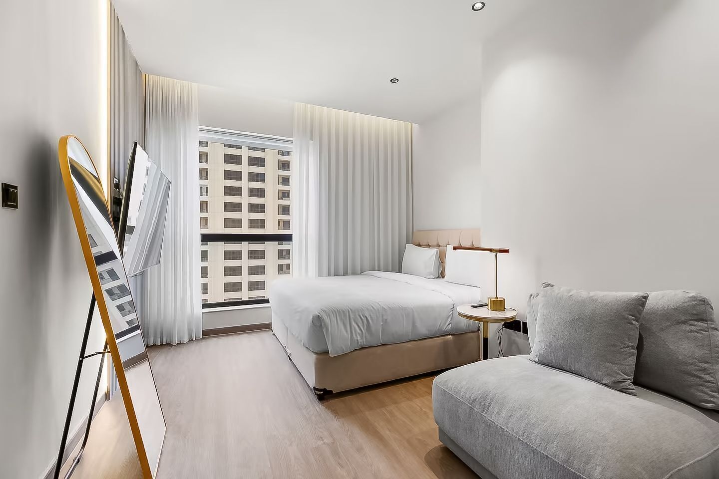 A modern hotel room with a bed, a sofa, a lamp, and a painting on the wall.