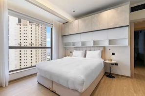A modern hotel room with a large bed, built-in shelving, and a view of high-rise buildings. - Murjan 2802 (Dubai)