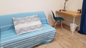 A room with a blue sofa, a wooden desk, a green chair, and a small trash bin. - B B Palazzo Zappala (Catania)