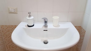 A white bathroom sink with a faucet, a soap dispenser, and a cup. - B B Palazzo Zappala (Catania)