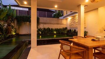 A modern outdoor dining area with a pool, wooden furniture, and decorative lighting.