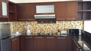 A kitchen with dark wooden cabinets, a tiled backsplash, a refrigerator, a blender, a toaster, and a microwave. - Juada Garden (Seminyak)