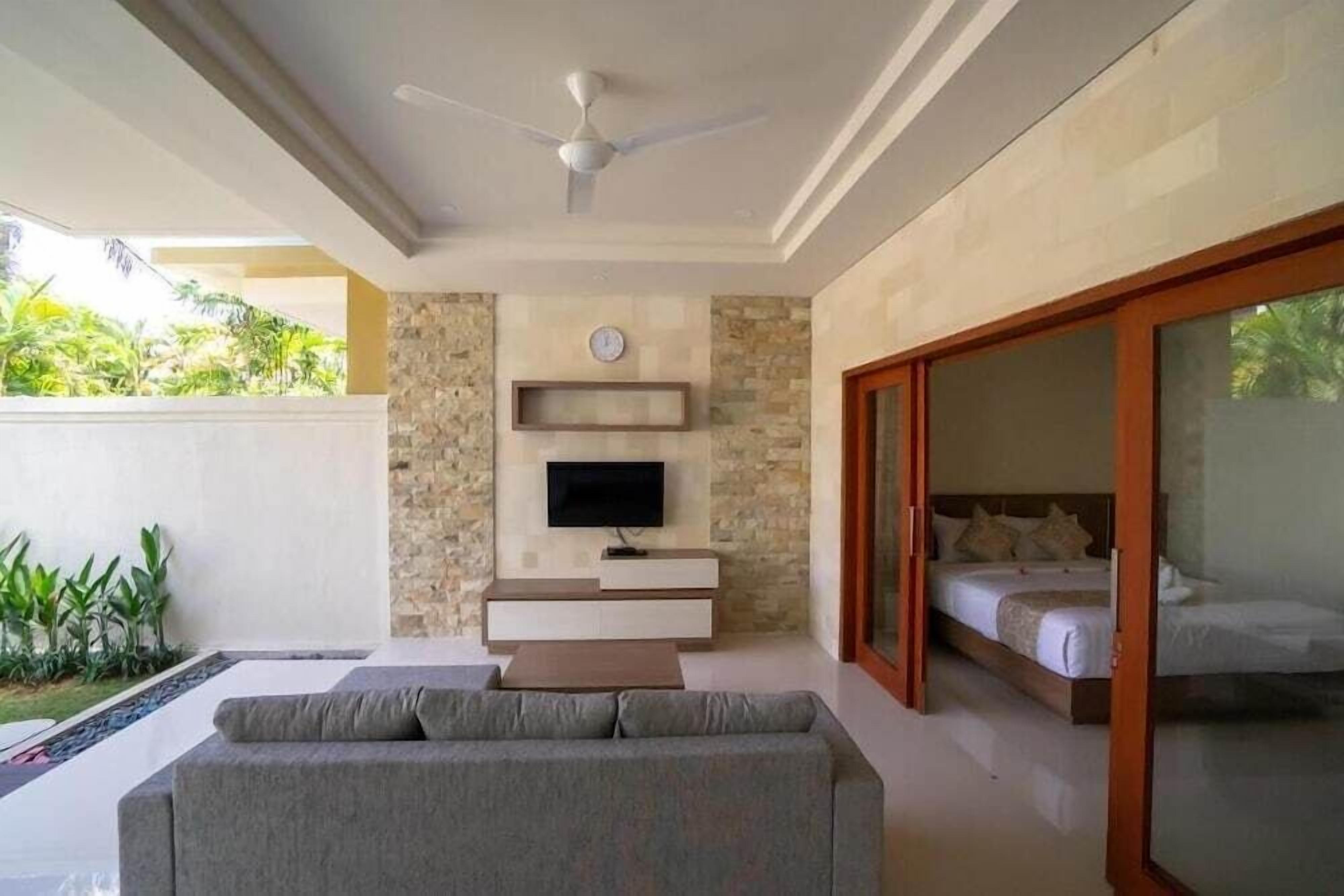A modern room with a sofa, a flat-screen TV, a bed, and a ceiling fan.