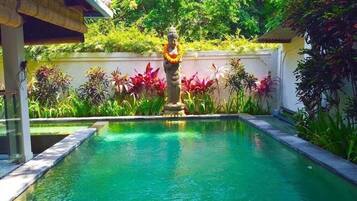 A swimming pool with a statue in the center, surrounded by lush greenery and a white wall.