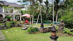 A tropical garden with a pool, stone statues, and a gazebo.