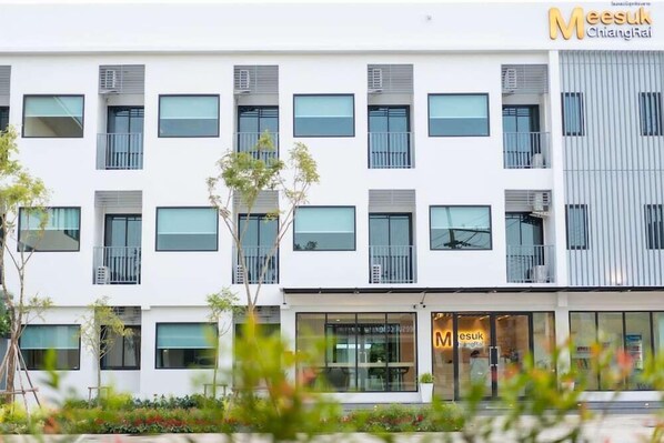 A modern multi-story building with a white facade, multiple balconies, and a storefront with signage. - Meesuk Residence (Chiang Rai)