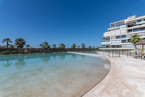 Ein modernes Hotel mit Pool, Palmen und blauem Himmel.