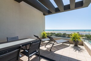 Ein Balkon mit Tisch und Stühlen, einem Blumentopf und Blick auf den Strand.