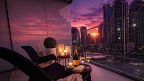 Un balcone con vista sul tramonto, una bottiglia di champagne, due calici, candele e un libro su un tavolino.