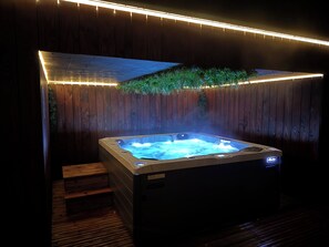 Un jacuzzi con un muelle de madera y escalones que llevan a él, rodeado por una cerca de madera y una guirnalda de luces.