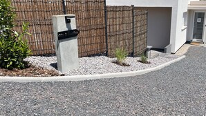 En indkørsel med grusbelægning, en betonstolpe med et sort skilt, et træhegn og en hvid garageport.