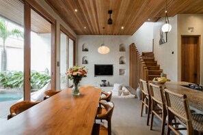 A modern dining area with a wooden table, chairs, and a TV mounted on the wall. - Serenity Villa Jimbaran (Bali)