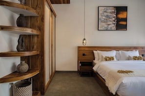 A bedroom with a wooden headboard, a bed with white bedding, a wall-mounted painting, and a hanging light fixture. - Serenity Villa Jimbaran (Bali)