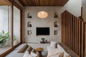 A modern living room with a flat-screen TV, wooden slat wall, and a sofa. - Serenity Villa Jimbaran (Bali)