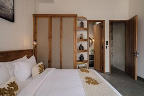 A bedroom with a bed, wooden wardrobe, and a shelf with decorative items. - Serenity Villa Jimbaran (Bali)
