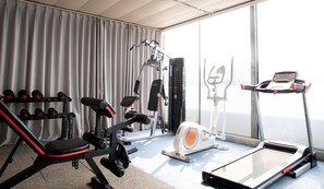 Une salle de sport équipée d’un tapis de course, d’un banc de musculation, d’haltères et d’autres appareils d’exercice.