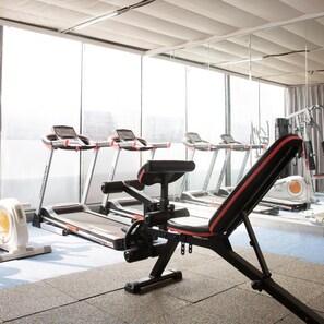 Une salle de sport équipée de tapis de course, d’un banc de développé couché et d’appareils de musculation.