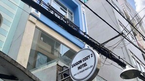 Une enseigne d’hôtel portant le nom « Saigon Cozy 2 Hotel » et l’adresse « 241/12 Pham Ngoc Lieu ».