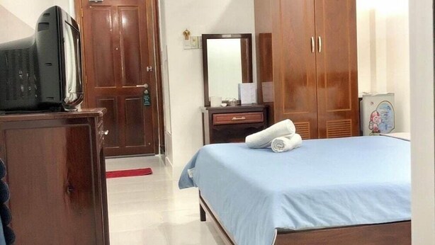 Une chambre à coucher avec un lit, une armoire en bois, un bureau avec un miroir et un téléviseur posé sur un meuble.